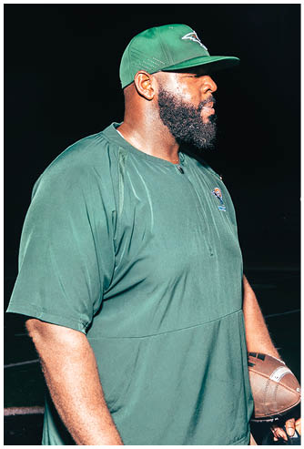 A person in a football uniform with a helmet and gloves is standing on a football field in a ready position during a game. Description generated by AI