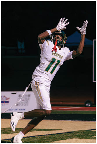 Two people in football uniforms are engaged in a tackle on a field during a game at night. Description generated by AI