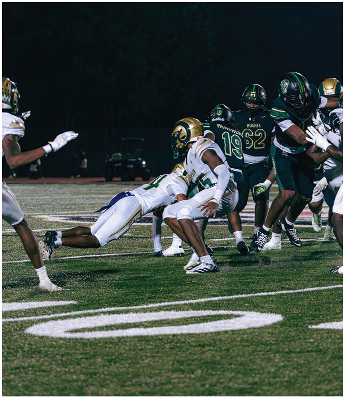 Two people in football uniforms and helmets are on a field with a referee standing behind them. Description generated by AI