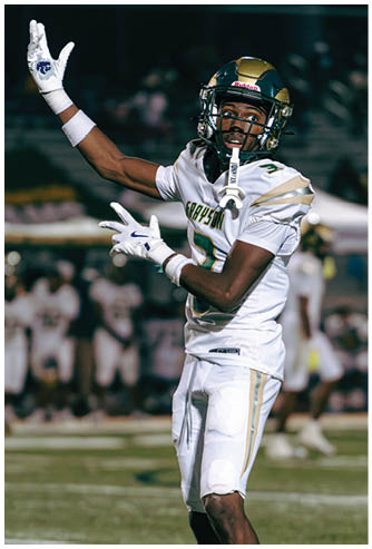 A person in a white and green football uniform with the name Grayson is running on a field holding a football while another person in similar attire stands nearby and a photographer captures the moment in the background. Description generated by AI