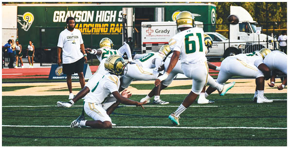 Two people wearing white sports uniforms with green and yellow stripes stand on a field with others in the background. Description generated by AI