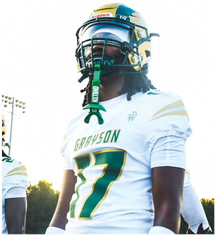 Two people in football uniforms celebrating on a field with a chain-link fence and a blue Academy Sports + Outdoors banner in the background. Description generated by AI