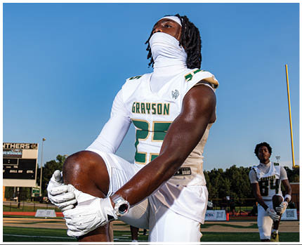 A person in a white football uniform with the number 13 is holding a football and preparing to make a play on a green field with yard lines. Description generated by AI