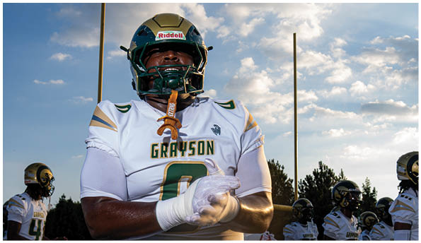 A person wearing a white football uniform and gold helmet is catching a football on a green field during a game. Description generated by AI