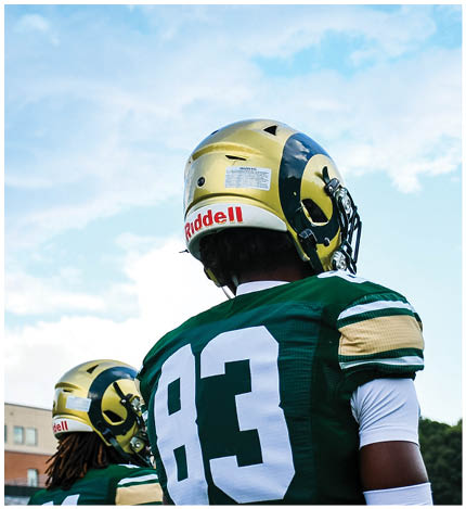 Two people in football uniforms celebrating on a field with a chain-link fence and a blue Academy Sports + Outdoors banner in the background. Description generated by AI