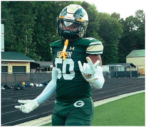 People in cheerleading uniforms hold a large white banner on a sports field that reads “THE BEST IN THE G GAME YOU KNOW THE NAME" with the letter G highlighted in green and gold. Description generated by AI