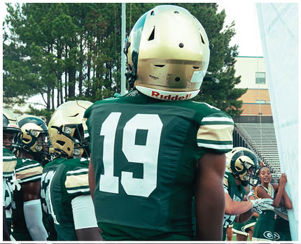 A person in a white football uniform with the number 13 is holding a football and preparing to make a play on a green field with yard lines. Description generated by AI