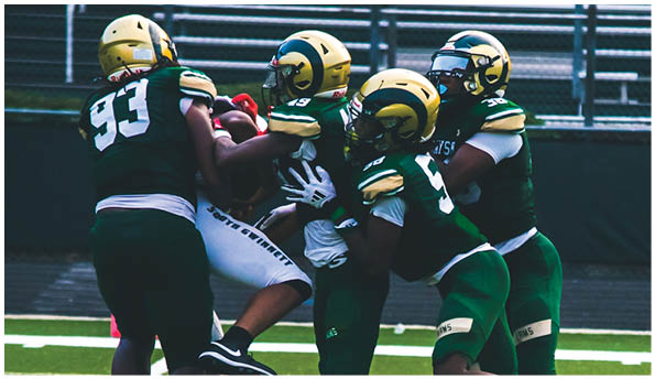 A person wearing a white football uniform and gold helmet is catching a football on a green field during a game. Description generated by AI
