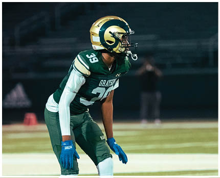 A person wearing a football helmet and white jersey is standing next to others in similar gear during a game or practice. Description generated by AI