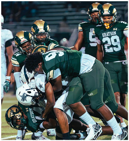 A person wearing a white football uniform with the number 12 is crouched in an athletic stance on a green turf field marked with white and yellow lines. Description generated by AI
