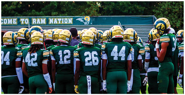 People wearing football helmets and uniforms are gathered closely on a field with a dark background. Description generated by AI
