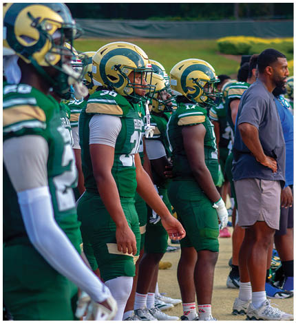 A person in a white football uniform with the name Grayson and number 39 is raising one arm and pointing with the other on a football field while other players and cheerleaders stand in the background. Description generated by AI