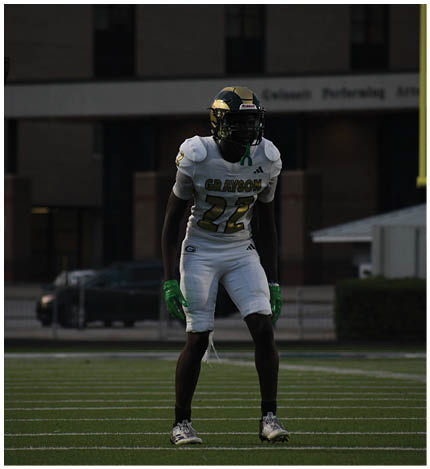 An adult wearing a green and white football uniform with the number 29 is running on a football field while two other adults stand nearby. Description generated by AI