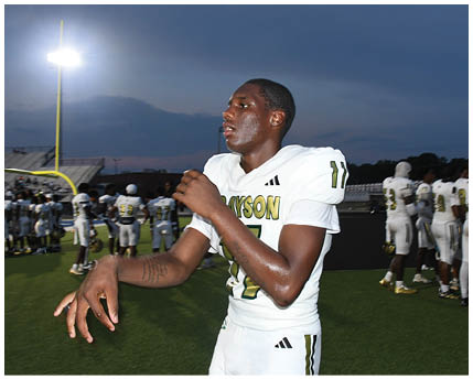 Two people in green and white football uniforms are standing on a field with one person bent forward and the other standing upright holding a football. Description generated by AI