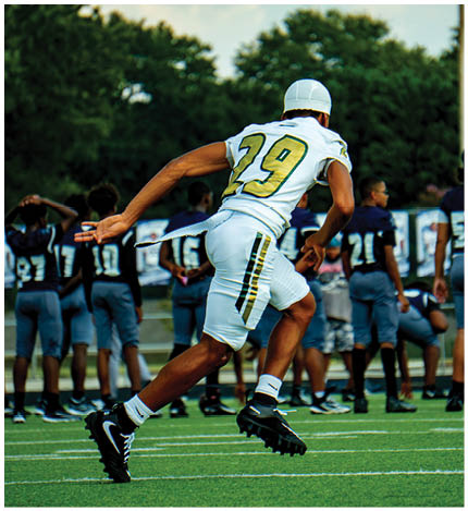 People wearing green and white football uniforms standing on a field, with one person gesturing with their hand. Description generated by AI
