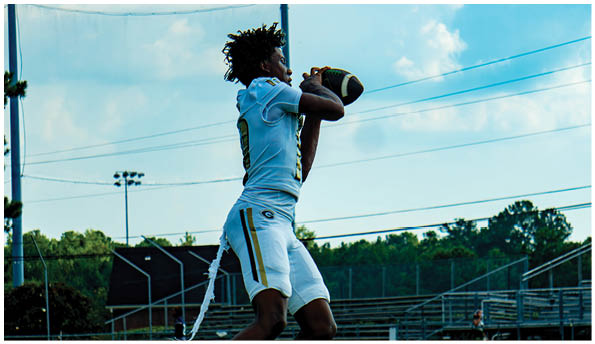 Two adults wearing sports apparel and sunglasses stand outdoors on a field with a referee visible in the background. Description generated by AI