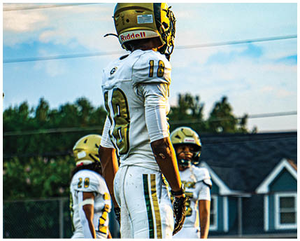 A person wearing a green football uniform with the name Grayson and number 20 is pointing forward on a football field. Description generated by AI