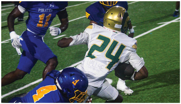 A person wearing a white football uniform and helmet is running with a football on a field while people in green cheerleading outfits stand in the background. Description generated by AI