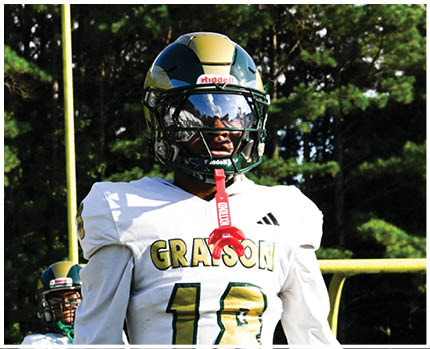 A person wearing a gold and black football helmet and a white jersey with the word “BRAVES" visible is looking to the side against a blue sky background. Description generated by AI