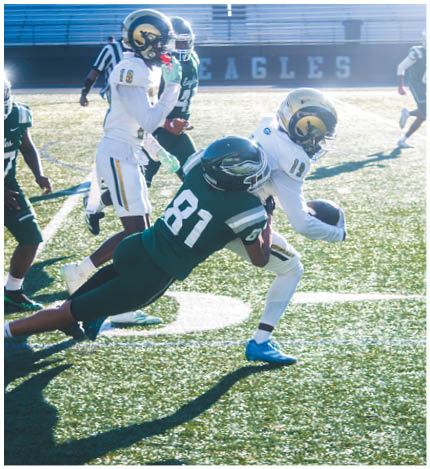 A person with long dreadlocks wearing a white football jersey with the name Grayson and the number 28 stands in front of two other people in similar football uniforms and helmets. Description generated by AI