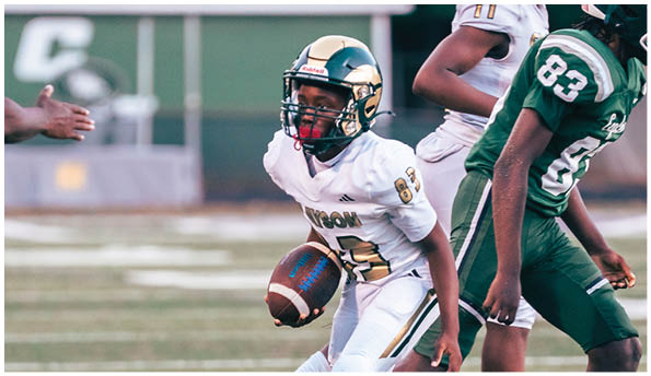 A person wearing white athletic pants and cleats is standing on a green football field with white yard lines. Description generated by AI