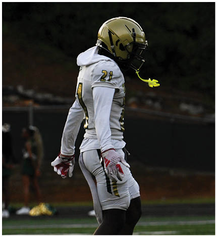 A person wearing a white football uniform with the number 13 is walking on a field toward a group of similarly dressed players standing on the sidelines. Description generated by AI