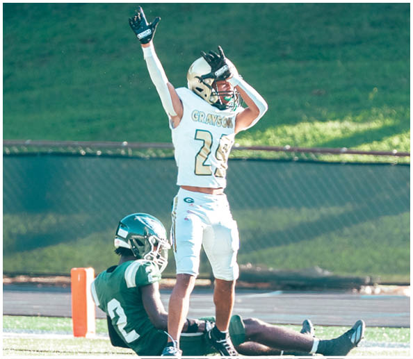 People in cheerleading uniforms hold a large white banner on a sports field that reads “THE BEST IN THE G GAME YOU KNOW THE NAME" with the letter G highlighted in green and gold. Description generated by AI