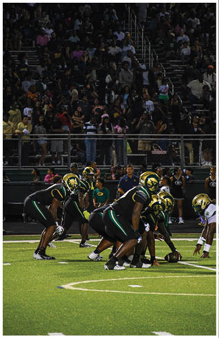 A person wearing white athletic pants and cleats is standing on a green football field with white yard lines. Description generated by AI