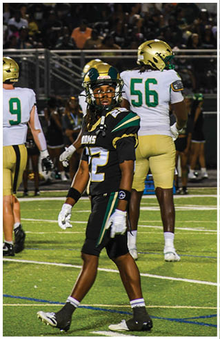 A person wearing white athletic pants and cleats is standing on a green football field with white yard lines. Description generated by AI