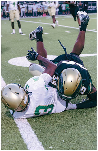 A person wearing white athletic pants and cleats is standing on a green football field with white yard lines. Description generated by AI