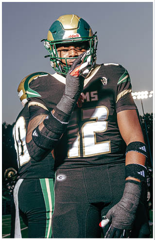 A person wearing white athletic pants and cleats is standing on a green football field with white yard lines. Description generated by AI
