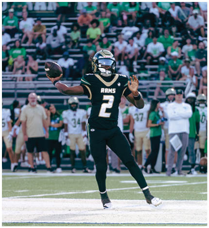 A person with long dreadlocks wearing a white football jersey with the name Grayson and the number 28 stands in front of two other people in similar football uniforms and helmets. Description generated by AI