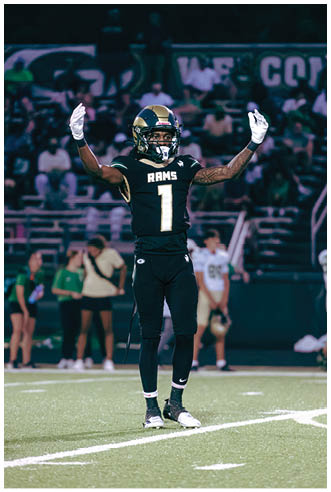 A person wearing white athletic pants and cleats is standing on a green football field with white yard lines. Description generated by AI