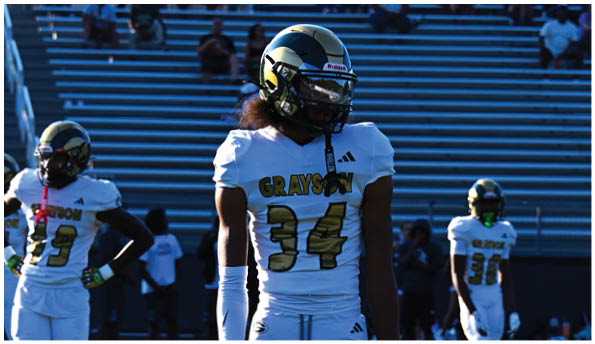 A person wearing white athletic pants and cleats is standing on a green football field with white yard lines. Description generated by AI