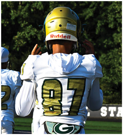 A person wearing a white football uniform with the number 13 is walking on a field toward a group of similarly dressed players standing on the sidelines. Description generated by AI
