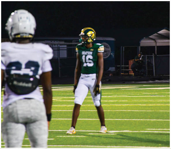 People in cheerleading uniforms hold a large white banner on a sports field that reads “THE BEST IN THE G GAME YOU KNOW THE NAME" with the letter G highlighted in green and gold. Description generated by AI
