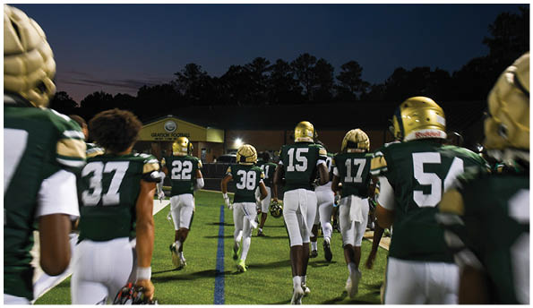 A person wearing a white football uniform and gold helmet is catching a football on a green field during a game. Description generated by AI