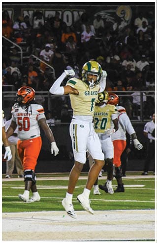 A person wearing white athletic pants and cleats is standing on a green football field with white yard lines. Description generated by AI