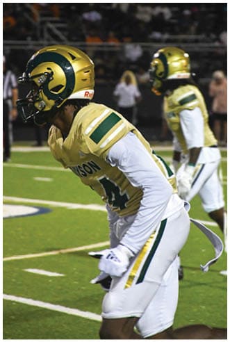 A person wearing white athletic pants and cleats is standing on a green football field with white yard lines. Description generated by AI