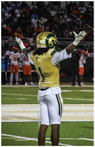 A person wearing white athletic pants and cleats is standing on a green football field with white yard lines. Description generated by AI
