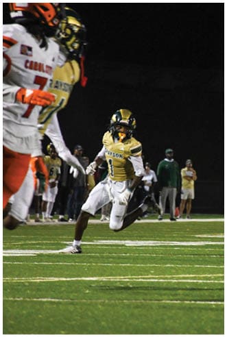 A person wearing white athletic pants and cleats is standing on a green football field with white yard lines. Description generated by AI