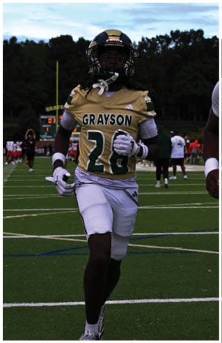 A person wearing white athletic pants and cleats is standing on a green football field with white yard lines. Description generated by AI