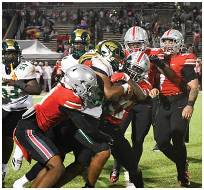 A group of people wearing football uniforms are on a field with one person in a white and green uniform standing in the center and others in red uniforms around them. Description generated by AI