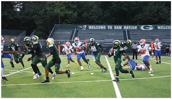 A person wearing white athletic pants and cleats is standing on a green football field with white yard lines. Description generated by AI