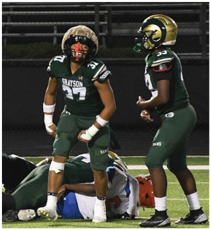 A person with long dreadlocks wearing a white football jersey with the name Grayson and the number 28 stands in front of two other people in similar football uniforms and helmets. Description generated by AI