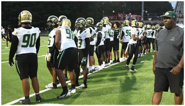 A person wearing white athletic pants and cleats is standing on a green football field with white yard lines. Description generated by AI