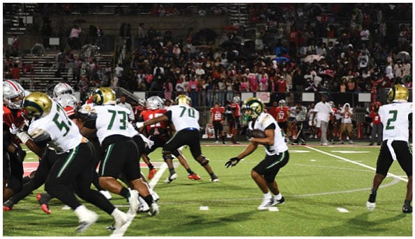 A person wearing white athletic pants and cleats is standing on a green football field with white yard lines. Description generated by AI