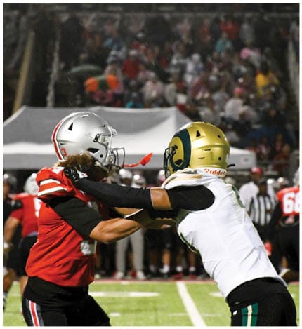 A person with long dreadlocks wearing a white football jersey with the name Grayson and the number 28 stands in front of two other people in similar football uniforms and helmets. Description generated by AI