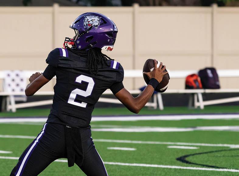 Four people wearing black football uniforms with “VISTA" on the front are standing together in a stadium with a crowd in the background, two of them holding helmets raised above their heads. Description generated by AI