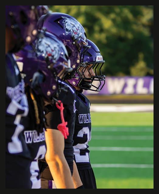 A person with curly hair wearing a black football uniform with “VISTA" on the jersey is sitting on a grassy field with one leg bent and the other extended. Description generated by AI